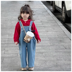 Detail of baby girl wearing a knitted bubble tea crossbody bag with denim overalls