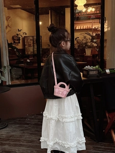 Close-up of pink quilted mini crossbody bag worn by a child in a retro cafe setting