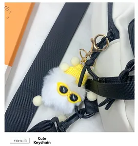 Gros plan d'un charme en peluche blanche avec lunettes et chapeau jaunes sur un sac