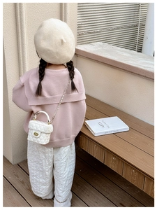Outdoor view of girl wearing a pink knit sweater with a quilted white crossbody bag