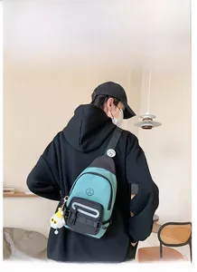 Détail du sac bandoulière bleu sarcelle et noir avec breloque et badge sur la sangle