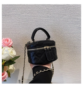 Mini black quilted crossbody bag with gold chain strap held by hand for scale