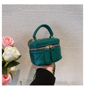 Detail of dark green quilted mini handbag with gold zippers and chain strap