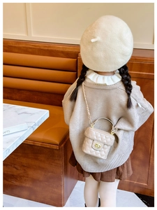 Detail of a beige quilted crossbody bag with a gold metal chain strap on a child model