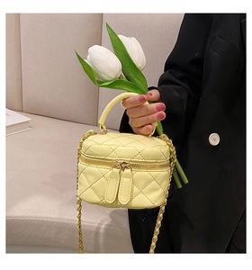 Detail of yellow quilted mini bag with chain strap held by a person in a black blazer