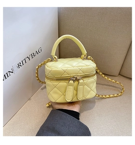 Detail of a mini yellow quilted leather vanity bag with gold chain strap and dual zippers