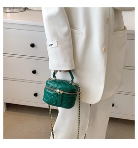 Detail of dark green quilted mini bag with gold chain strap held by a model