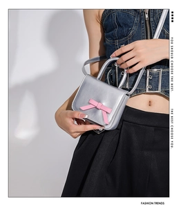 Detail of mini silver metallic handbag featuring a prominent pink bow and slim strap