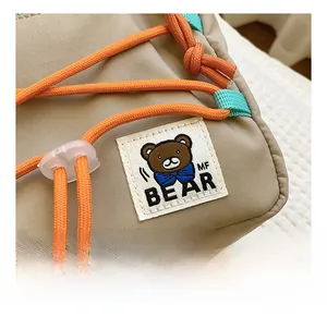 Detail of khaki nylon kid's bag with orange drawstring and cute brown MF BEAR patch