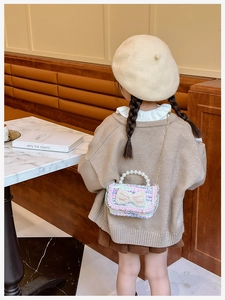 Close-up of children's woven handbag with pearl bow detail and gold chain strap