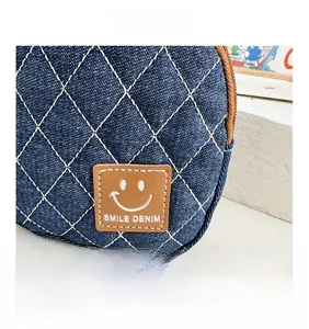 Dettaglio borsa in denim trapuntata con toppa smile in pelle marrone e cerniera lampo