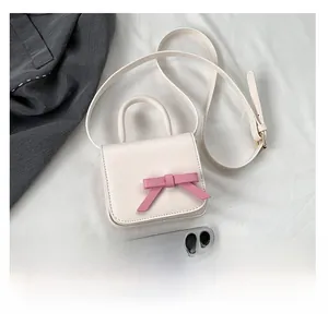 Mini cream crossbody bag with pink bow detail shown next to a smartphone for scale
