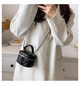 Close-up of black quilted mini bag with gold chain strap on white blazer outfit