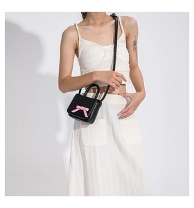 Mini black leather bag with pink bow accent worn with stylish white textured outfit