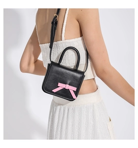 Detailed close-up of a mini black crossbody bag with a stylish pink bow and leather strap