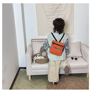 Side view of a child wearing the orange Freedom printed backpack in a cozy home setting