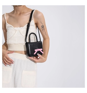 Mini black leather crossbody bag with pink bow detail shown on model for size reference