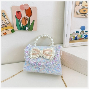 Detail of tweed girl's mini bag featuring pearl bow, lace trim, and beaded handle