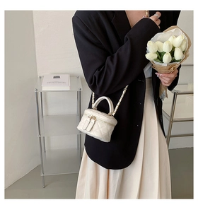 Detail shot of a white quilted crossbody vanity bag with gold chain and top handle