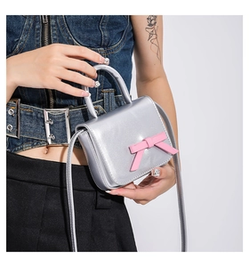 Mini silver crossbody bag with a pink bow detail held by a model in denim