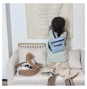 Detail of light blue canvas kids backpack with Freedom lettering shown on a child's back