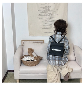 Detail of a black kids Freedom letter backpack with adjustable straps on a soft beige sofa