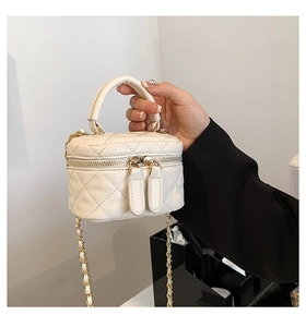 Close-up of cream quilted mini vanity bag with gold chain strap held by a model