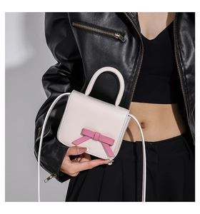 Detailed view of mini cream crossbody bag with pink bow accessory and leather strap