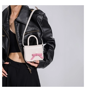 Mini cream leather crossbody bag with pink bow accent worn by model in black jacket
