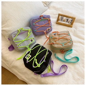 Flat lay of nylon kids crossbody bags in four colors with bungee cord and bear patch
