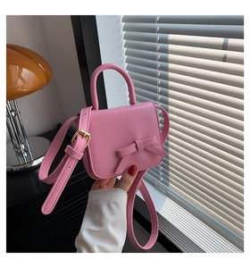 Pink bow mini crossbody bag with gold hardware held against a stylish lifestyle background