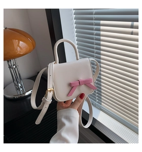 Close-up of a mini cream leather crossbody bag with a cute pink bow and adjustable strap