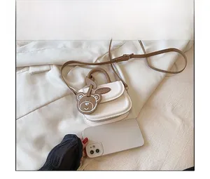 Mini borsa a tracolla bimba panna in pelle con ciondolo orsetto accanto a un telefono