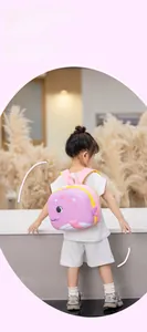 Pink cartoon whale-shaped EVA hardshell backpack shown on a child in a home setting