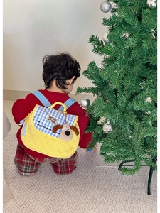 Toddler wearing yellow quilted puppy backpack near a decorated Christmas tree background