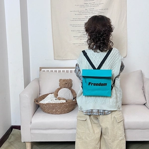 Kid's green dual-use crossbody backpack with Freedom lettering shown in a cozy home setting
