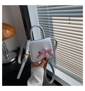 Detail of silver mini crossbody bag featuring a pink bow decoration and top handle