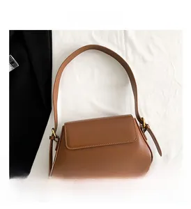 Detailed close-up of brown leather shoulder bag with flap closure on white fabric