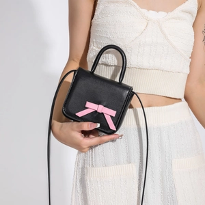 Mini black crossbody bag with pink bow on white textured outfit worn by model