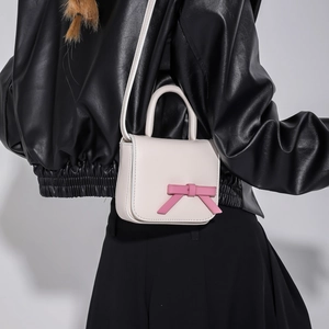 Mini crossbody bag with pink bow accent and cream leather texture on female model
