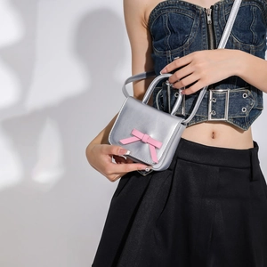 Silver mini crossbody bag featuring a pink bow accent shown by hand-held model