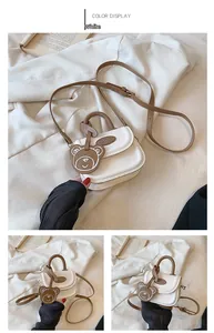 Dettaglio di una mini borsa a mano bianco crema con ciondolo a orso e tracolla lunga