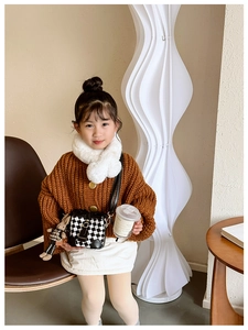 Close-up of a child's winter outfit with knit cardigan and checkerboard bucket bag