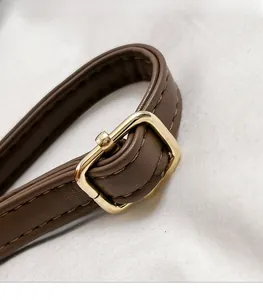Détail de la bandoulière en cuir marron foncé avec boucle en métal doré et couture fine