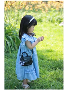 Foto all'aperto di una ragazza in abito blu con mini borsa a tracolla in pelle nera e orsetto