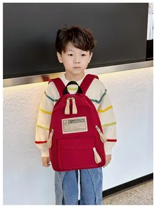 Détail du sac à dos enfant en nylon rouge avec grande poche avant et étiquette mode