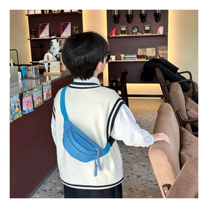 Blue canvas chest bag for kids shown from a side view on a child model in a cafe