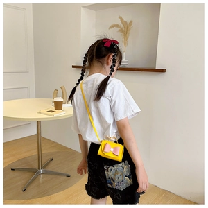 Detail showing the mini crossbody bag size on child with yellow PU and pink bow