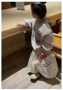 Détail d'un sac à main matelassé pour enfant avec broderie cerise et tenue beige