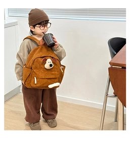 Close-up of brown corduroy kids backpack featuring a cute plush puppy and bone detail
